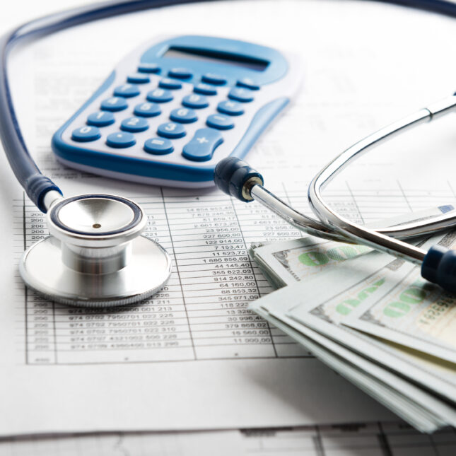 A stethoscope lays on banknotes next to a calculator, all on top of a insurance application form — business coverage from STAT