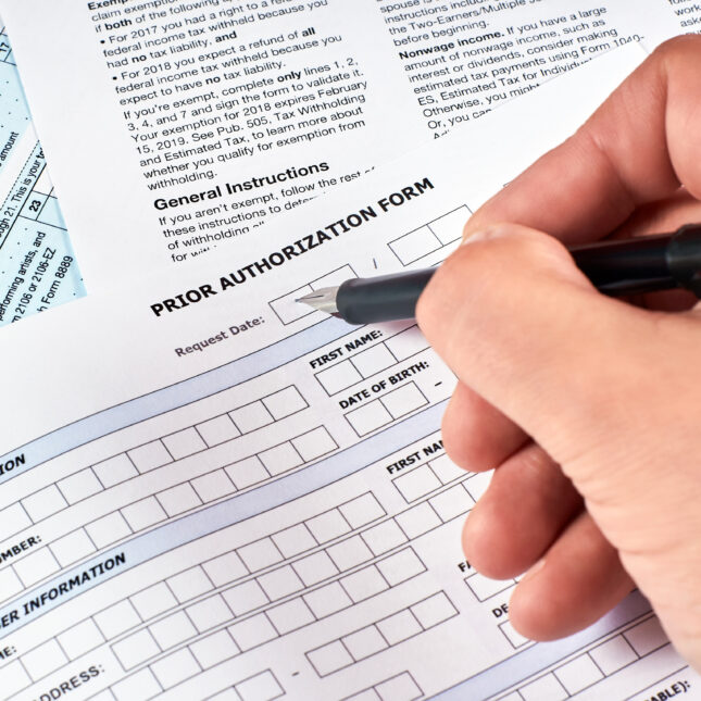 Holding a pen, a person starts to fill a blank prior authorization form -- first opinion coverage from STAT