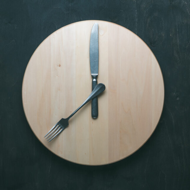 empty wooden round tray with a fork and butter knife as clock hands. -- biotech coverage from STAT
