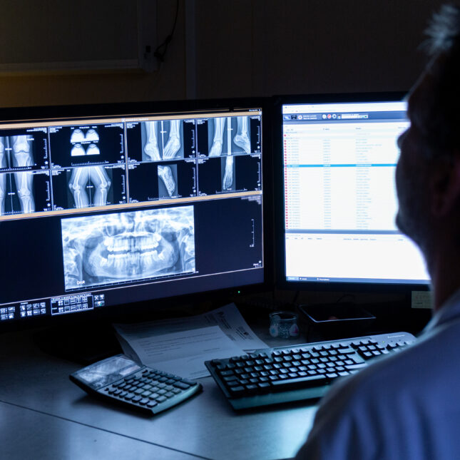 A radiologist looks at X-rays on screen in a dark room — coverage from STAT
