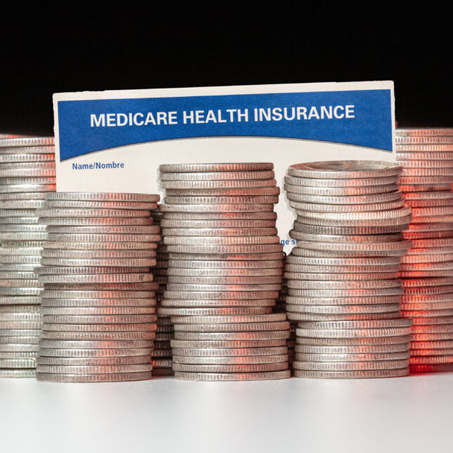 Stacks of silver coins surrounded by a medicare health insurance card — insurance coverage from STAT