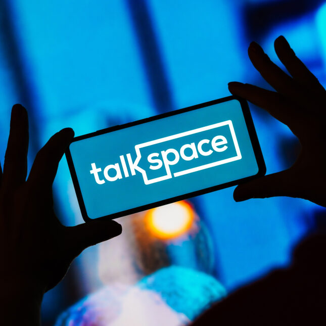 A Talkspace logo was displayed on a smartphone held by two hands — health tech coverage from STAT