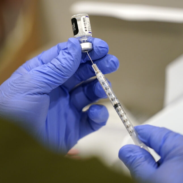 A healthcare worker in purple gloves fills a syringe with COVID-19 vaccine — health coverage from STAT