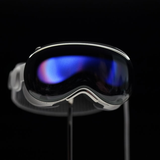 The Apple Vision Pro headset is displayed in a showroom against a black background.