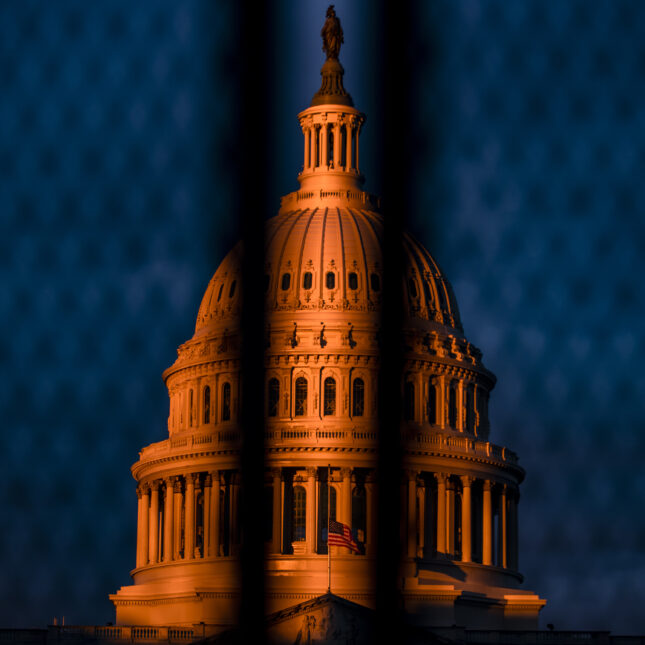 The dome of the U.S. Capitol in orange sun light behind a gate — health coverage from STAT