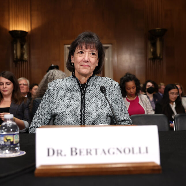 Doctor Monica Bertagnolli, a white woman with short hair and bangs, sits at a hearing behind her name tag — health policy coverage from STAT
