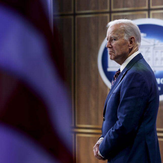 U.S. President Joe Biden stands with his fingers locked next to an US flag — politics coverage from STAT