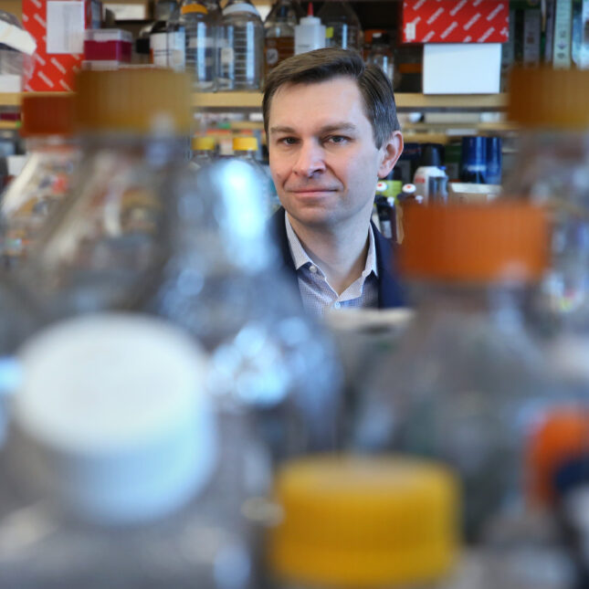 In a lab at Harvard Medical School, Professor David A. Sinclair looks into the camera from behind a row of bottles — coverage from STAT